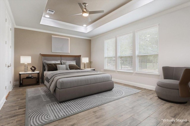 bedroom with visible vents, ornamental molding, a tray ceiling, and wood finished floors