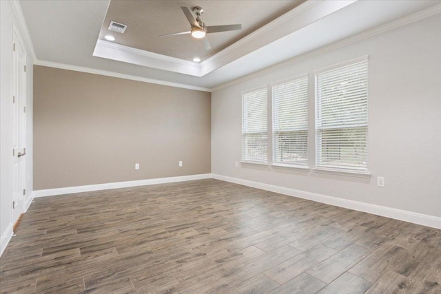 spare room featuring wood finished floors, visible vents, a tray ceiling, ceiling fan, and crown molding