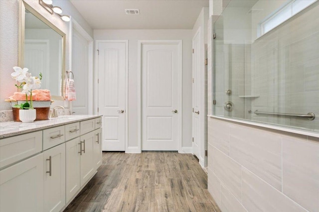 full bathroom with vanity, wood finished floors, baseboards, visible vents, and tiled shower