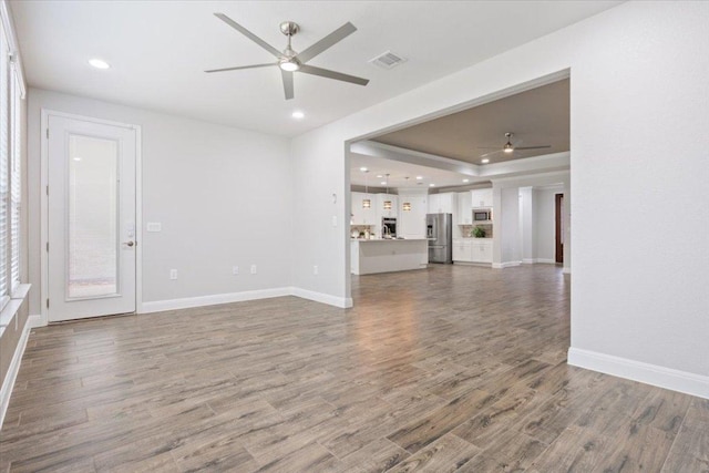 unfurnished living room with wood finished floors, visible vents, baseboards, recessed lighting, and a raised ceiling