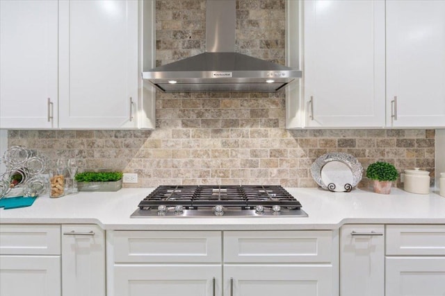 kitchen featuring stainless steel gas stovetop, wall chimney exhaust hood, white cabinets, light countertops, and decorative backsplash