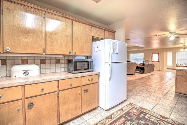 kitchen featuring decorative backsplash, stainless steel microwave, light countertops, and freestanding refrigerator