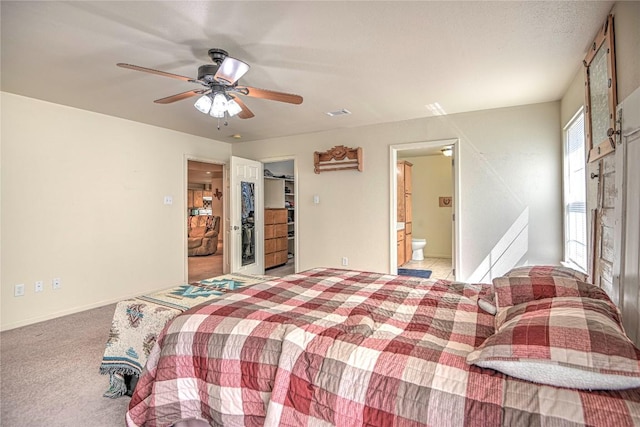 bedroom featuring a walk in closet, ensuite bathroom, a closet, light colored carpet, and ceiling fan