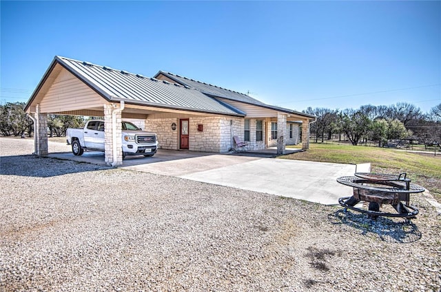 view of front facade featuring a fire pit, metal roof, stone siding, driveway, and a standing seam roof