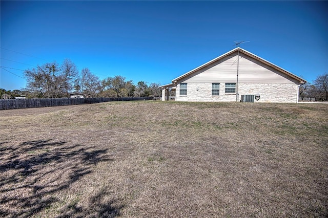 view of side of property featuring stone siding, a lawn, and fence