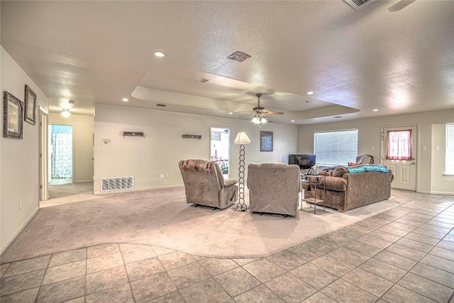 living room with a raised ceiling, visible vents, baseboards, and a textured ceiling