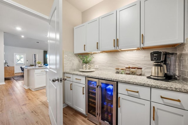 kitchen featuring light wood-type flooring, backsplash, wine cooler, white cabinets, and light stone countertops