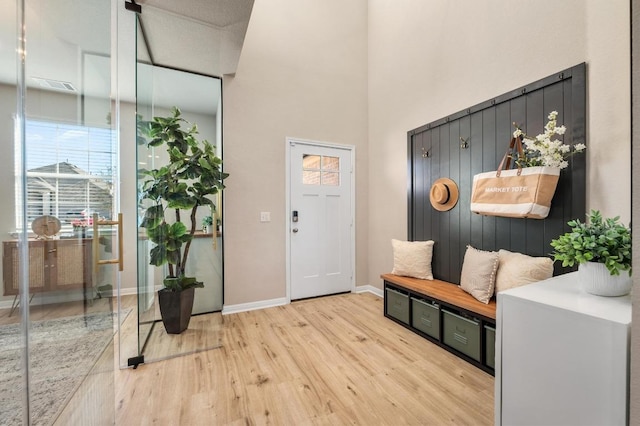 foyer with light wood-style flooring, baseboards, and a towering ceiling