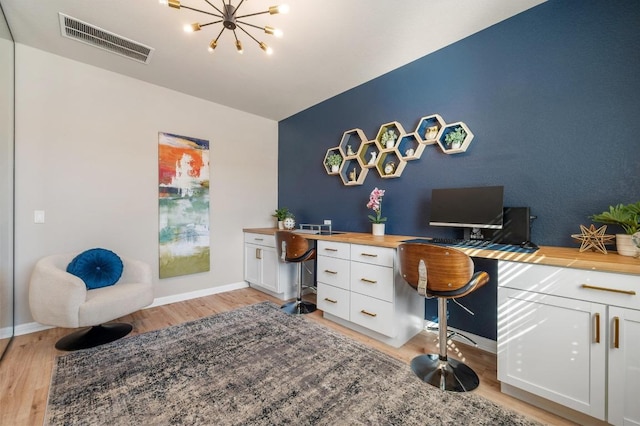 office space with baseboards, visible vents, an inviting chandelier, light wood-style flooring, and an accent wall