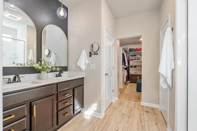 bathroom featuring a shower stall, wood finished floors, a walk in closet, and a sink