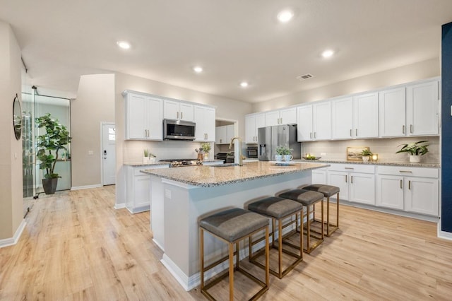 kitchen with visible vents, an island with sink, a sink, stainless steel appliances, and white cabinets