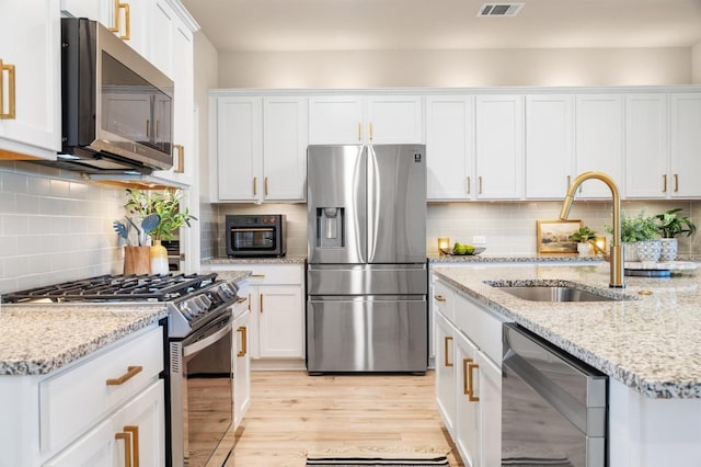 kitchen with a sink, tasteful backsplash, stainless steel appliances, light wood-style floors, and white cabinets