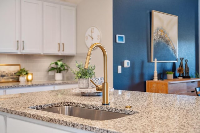 room details with a sink, decorative backsplash, light stone counters, and white cabinets