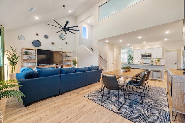 dining room featuring stairway, visible vents, light wood finished floors, high vaulted ceiling, and ceiling fan