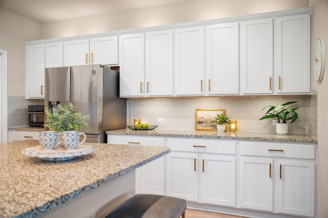 kitchen featuring tasteful backsplash, white cabinets, stainless steel refrigerator with ice dispenser, and light stone countertops