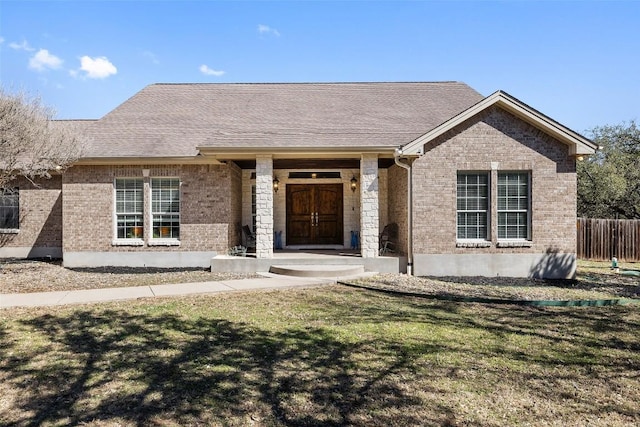 view of front facade with a front lawn, fence, brick siding, and a shingled roof