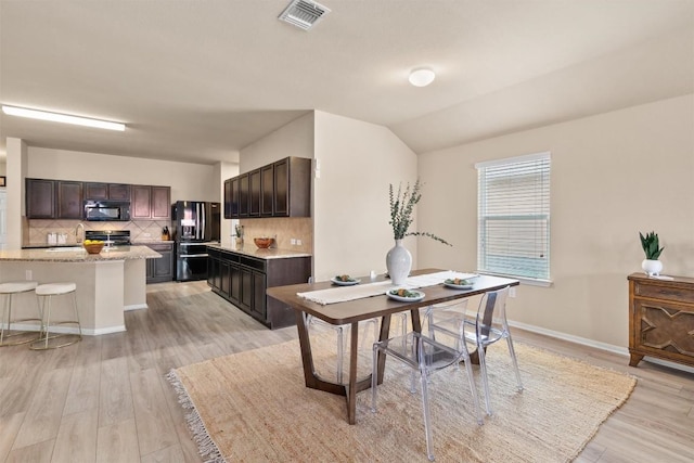 dining room featuring visible vents, baseboards, lofted ceiling, and light wood-style floors