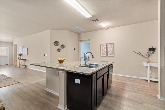 kitchen with light wood-style flooring, visible vents, a kitchen island with sink, and a sink