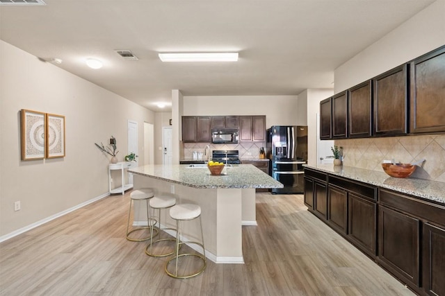 kitchen featuring dark brown cabinets, black appliances, and light wood-style flooring