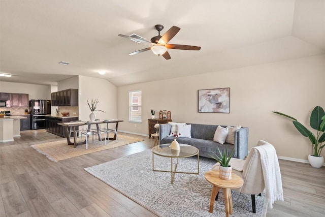 living area with ceiling fan, baseboards, light wood-style floors, and vaulted ceiling