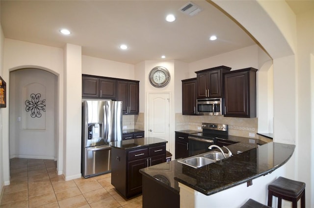 kitchen featuring arched walkways, stainless steel appliances, dark stone counters, and a sink