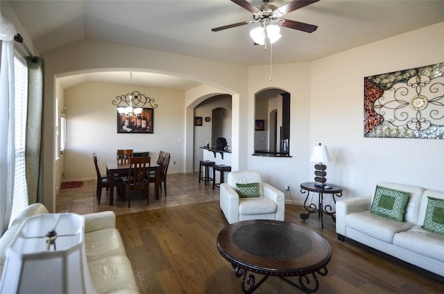 living room featuring baseboards, lofted ceiling, ceiling fan with notable chandelier, wood finished floors, and arched walkways