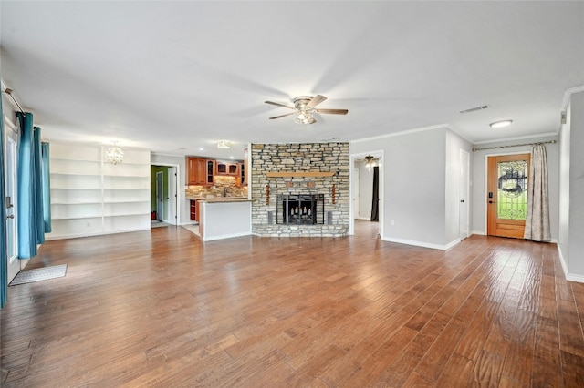 unfurnished living room featuring visible vents, wood finished floors, a stone fireplace, crown molding, and ceiling fan