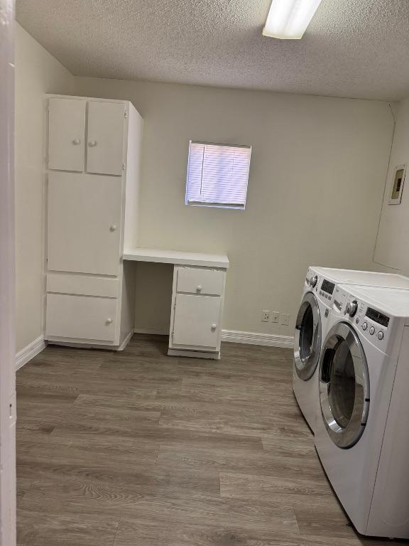 washroom with washing machine and clothes dryer, baseboards, light wood-type flooring, cabinet space, and a textured ceiling