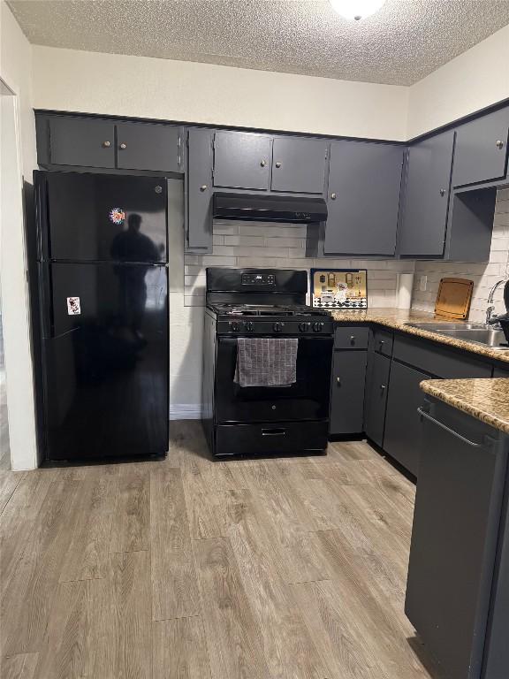 kitchen featuring backsplash, black appliances, under cabinet range hood, light wood-style flooring, and a textured ceiling