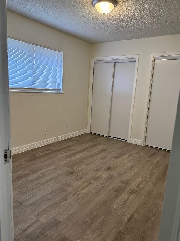 unfurnished bedroom with a closet, baseboards, a textured ceiling, and wood finished floors