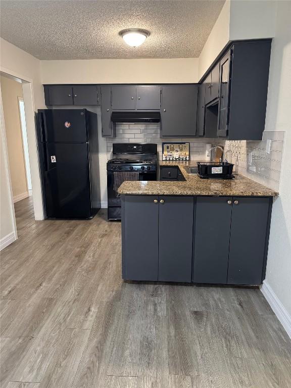 kitchen with black appliances, under cabinet range hood, tasteful backsplash, a peninsula, and light wood finished floors