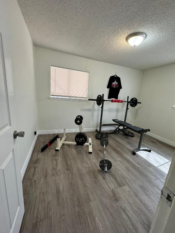 exercise area featuring wood finished floors, baseboards, and a textured ceiling