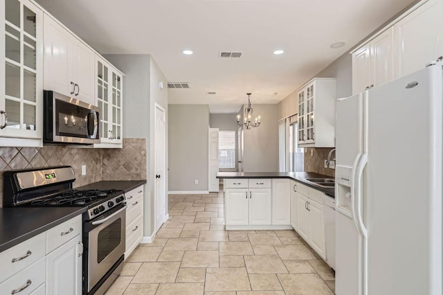 kitchen with a peninsula, a sink, glass insert cabinets, appliances with stainless steel finishes, and dark countertops