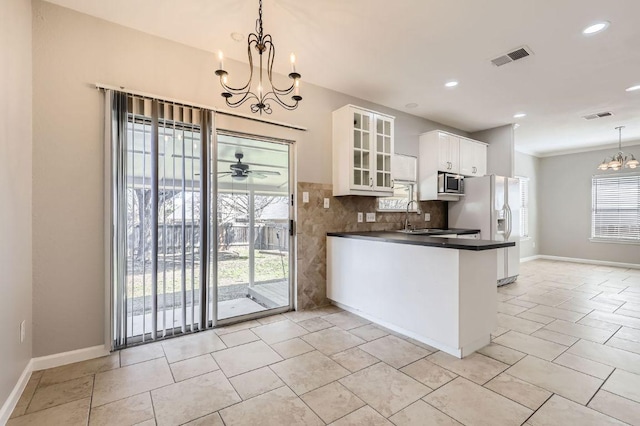 kitchen with dark countertops, stainless steel microwave, visible vents, ceiling fan with notable chandelier, and white fridge with ice dispenser