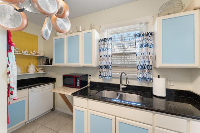 kitchen with light tile patterned floors, white cabinetry, dark stone counters, a sink, and dishwasher