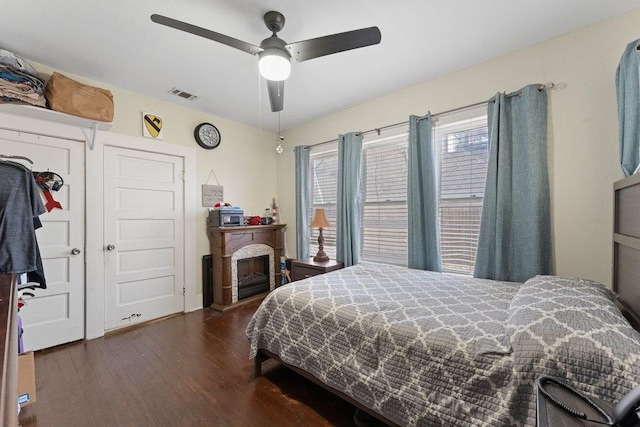 bedroom featuring dark wood finished floors, visible vents, a fireplace, and ceiling fan