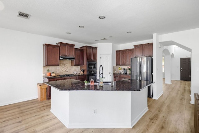 2246 Garlic Creek Dr, Buda, TX 78610 - kitchen with black appliances, arched walkways, light wood finished floors, dark stone counters, and recessed lighting