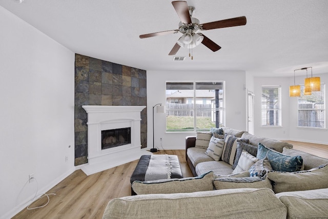 living area with a ceiling fan, baseboards, visible vents, light wood-type flooring, and a large fireplace