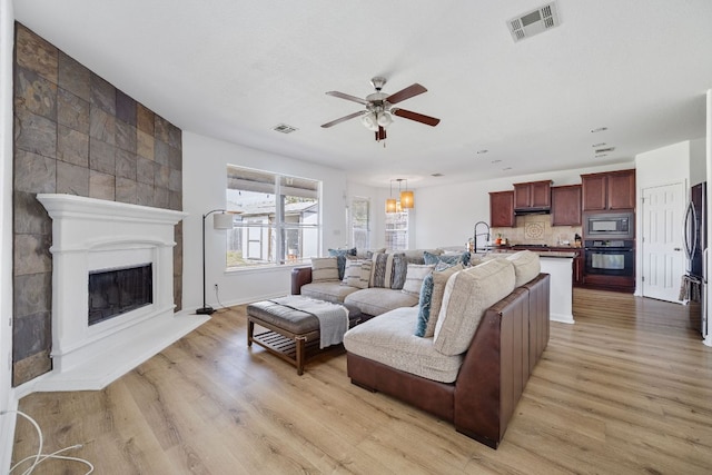 living room featuring ceiling fan, visible vents, light wood finished floors, and a large fireplace