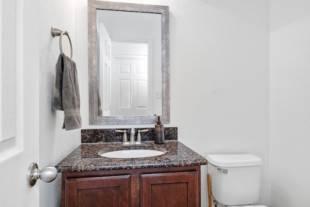 bathroom with toilet, vanity, and a textured wall