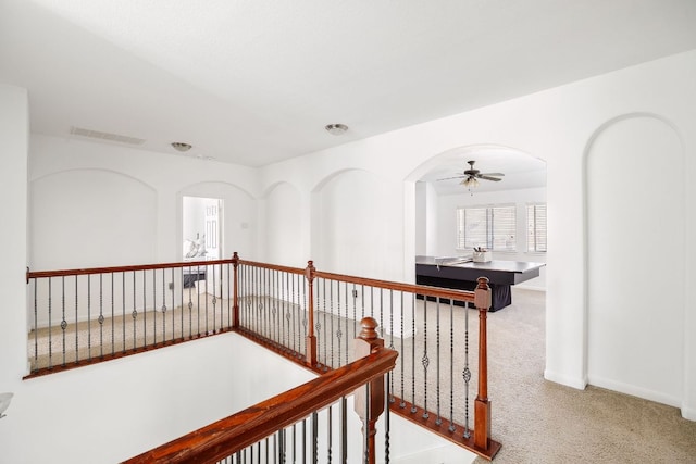 corridor featuring carpet, baseboards, visible vents, arched walkways, and an upstairs landing