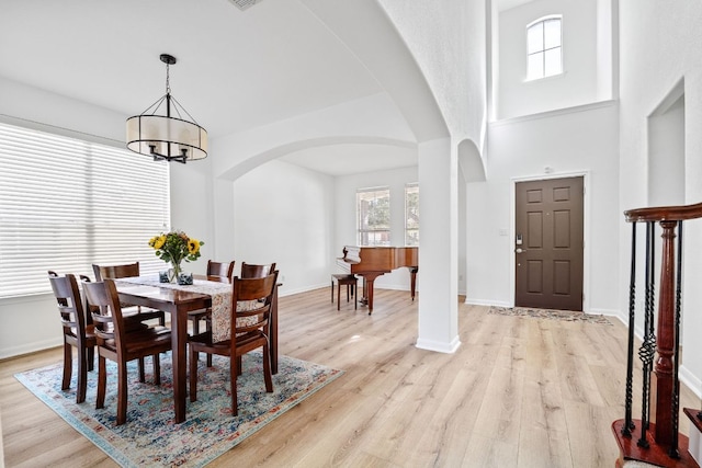 dining area featuring baseboards, a chandelier, light wood-style floors, a towering ceiling, and arched walkways