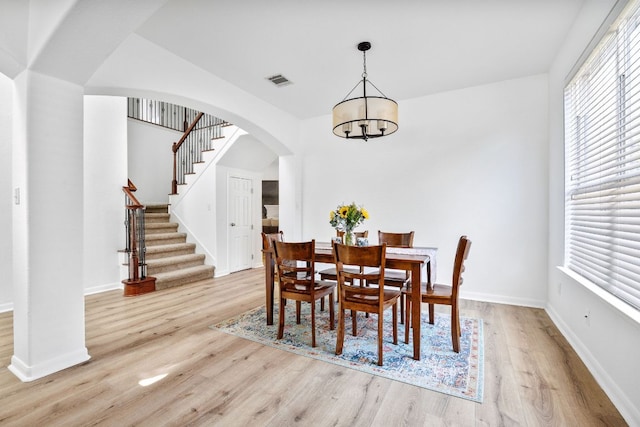 dining area with visible vents, arched walkways, light wood-style floors, and stairway