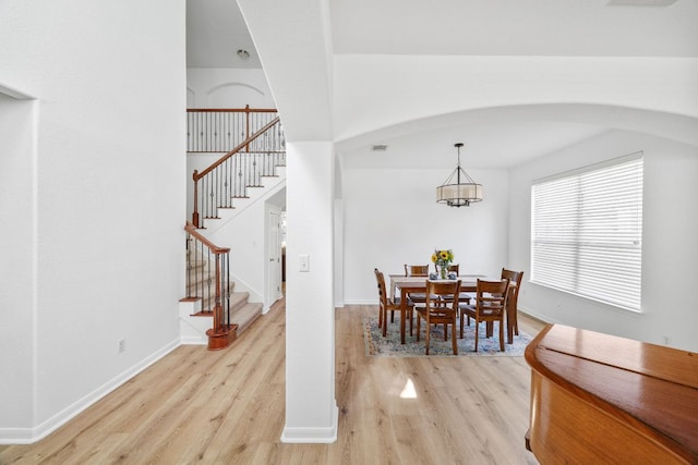 dining area featuring stairs, a notable chandelier, baseboards, and light wood finished floors