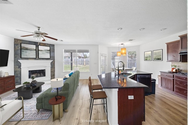 2246 Garlic Creek Dr, Buda, TX 78610 - kitchen with an island with sink, light wood-style floors, a ceiling fan, a kitchen bar, and a textured ceiling
