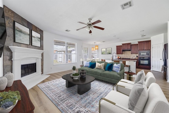 2246 Garlic Creek Dr, Buda, TX 78610 - living room featuring ceiling fan, light wood finished floors, a large fireplace, and a chandelier