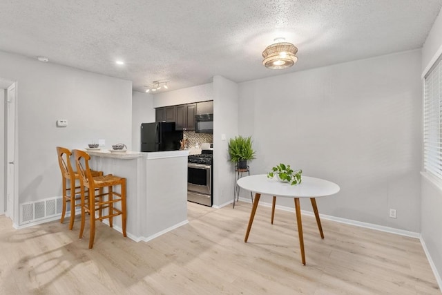 kitchen featuring visible vents, a breakfast bar area, light wood-type flooring, a peninsula, and black appliances