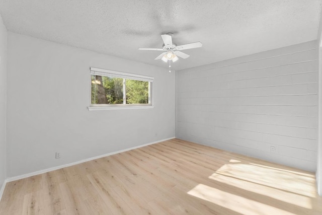 empty room with baseboards, wood finished floors, a textured ceiling, concrete block wall, and a ceiling fan