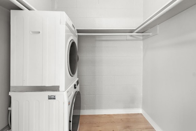 clothes washing area featuring baseboards, stacked washer and dryer, laundry area, wood finished floors, and concrete block wall