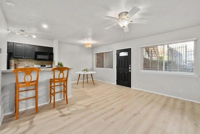 kitchen featuring a textured ceiling, tasteful backsplash, black microwave, light wood finished floors, and dark cabinets